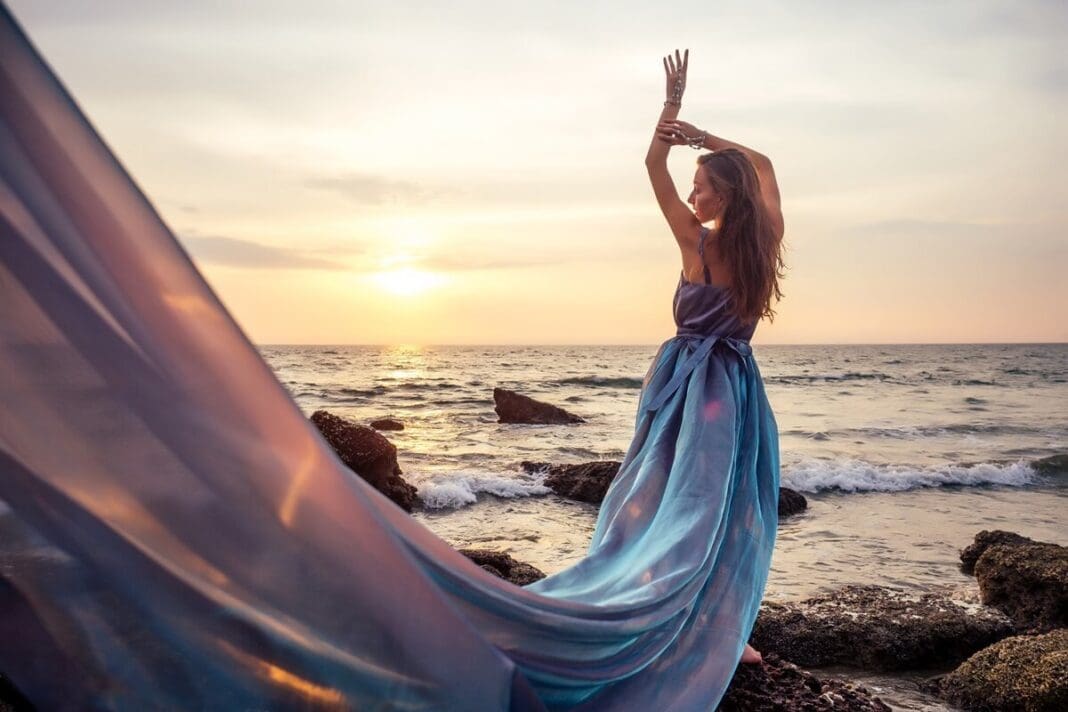 Young woman in blue chameleon dress standing on a rock near the sea